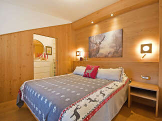 Experience rustic charm in this beautifully appointed bedroom, featuring warm wood paneling and a cozy queen-sized bed adorned with a festive reindeer-themed blanket.