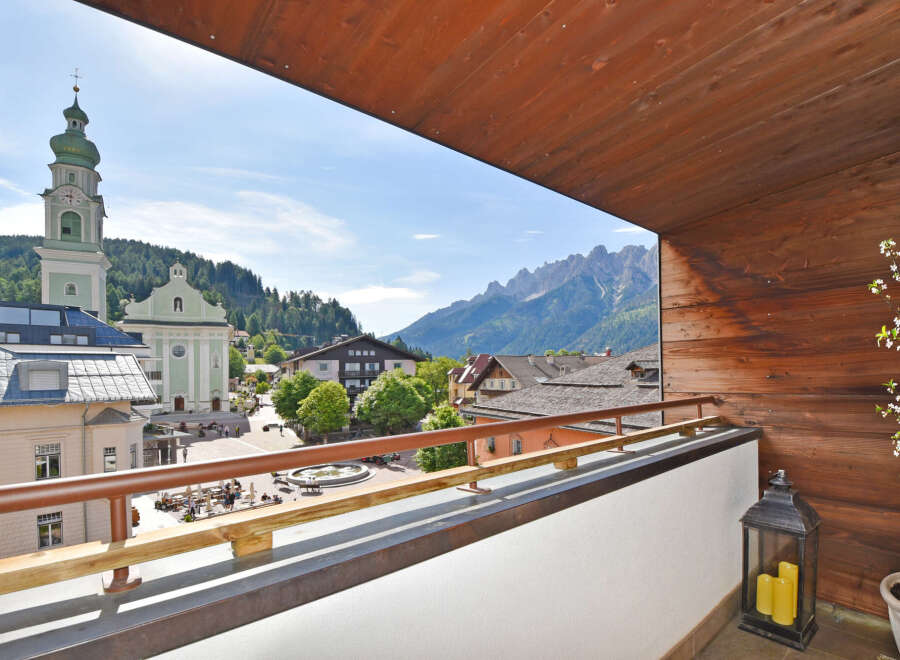 Experience breathtaking mountain views from this charming balcony, overlooking a picturesque town square with a historic church.