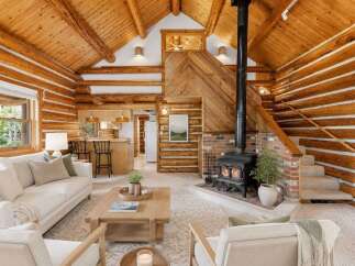 Experience rustic charm in this stunning log cabin living room, featuring a cozy fireplace and a beautiful wood-paneled ceiling.