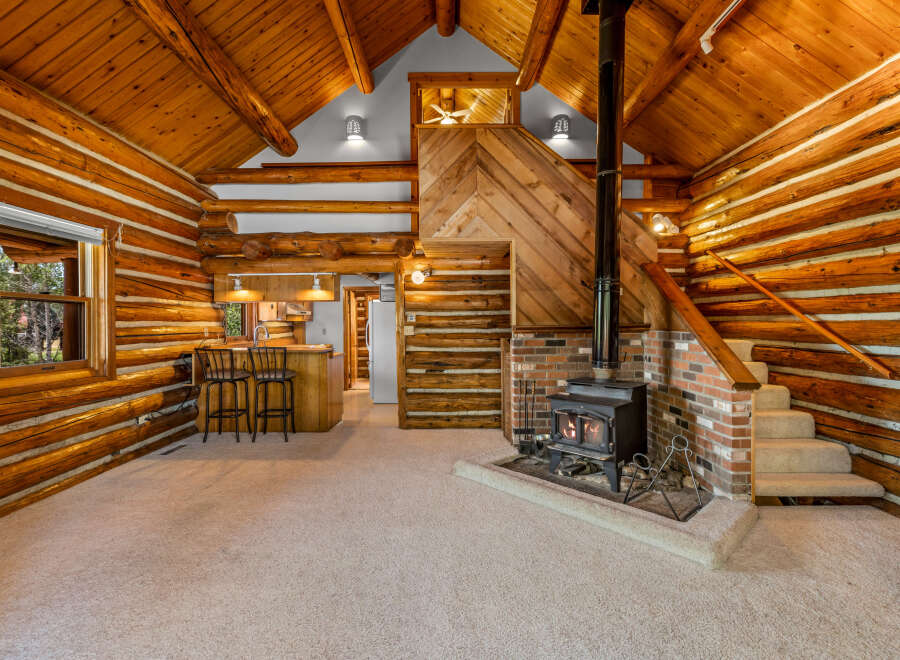 Experience rustic charm in this cozy log cabin living space, featuring a warm wood interior and a prominent stone fireplace with a wood-burning stove.
