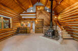 Experience rustic charm in this cozy log cabin living space, featuring a warm wood interior and a prominent stone fireplace with a wood-burning stove.