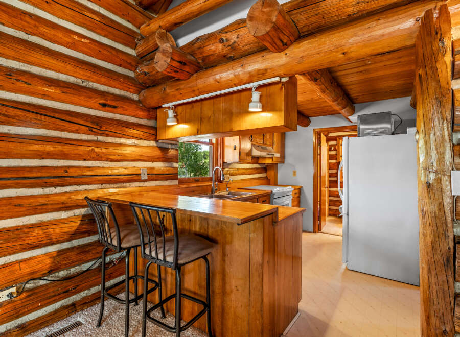 Experience rustic charm in this log cabin kitchen, featuring a cozy breakfast bar with two stools perfect for morning coffee.