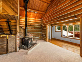 Experience rustic charm in this cozy log cabin living room, featuring a prominent wood-burning stove set against a brick hearth.