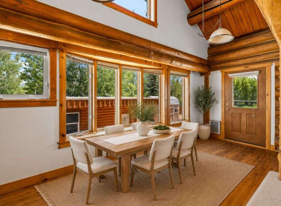 Experience rustic charm in this log cabin dining room, featuring a substantial wooden dining table surrounded by comfortable upholstered chairs.