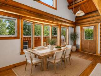 Experience rustic charm in this log cabin dining room, featuring a substantial wooden dining table surrounded by comfortable upholstered chairs.