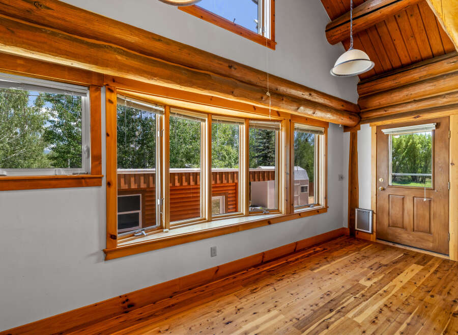Experience rustic charm in this log cabin interior, featuring a stunning bay window that floods the space with natural light and offers picturesque views of the surrounding greenery.