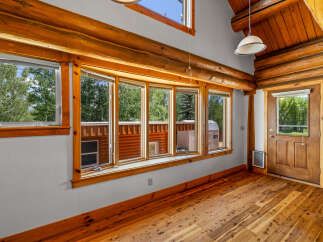 Experience rustic charm in this log cabin interior, featuring a stunning bay window that floods the space with natural light and offers picturesque views of the surrounding greenery.