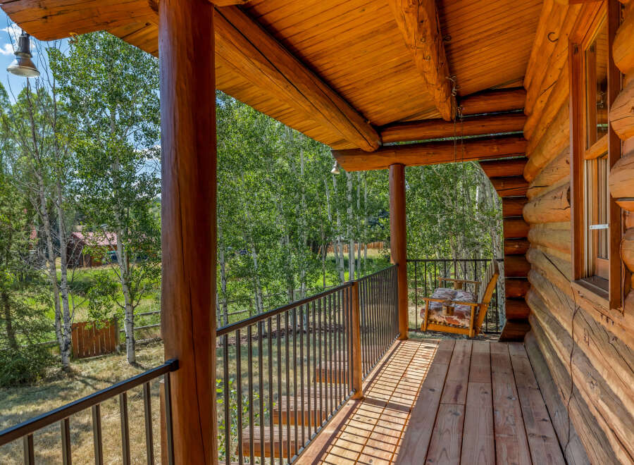 Experience rustic charm on this inviting log cabin porch, featuring a wooden swing chair perfect for enjoying the serene forest views.