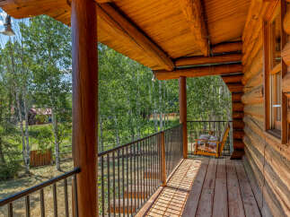 Experience rustic charm on this inviting log cabin porch, featuring a wooden swing chair perfect for enjoying the serene forest views.