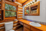 Experience rustic charm in this log cabin bathroom, featuring a bright orange vanity and a large window overlooking a serene forest.