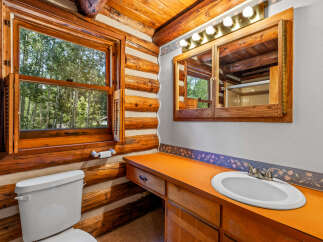 Experience rustic charm in this log cabin bathroom, featuring a bright orange vanity and a large window overlooking a serene forest.