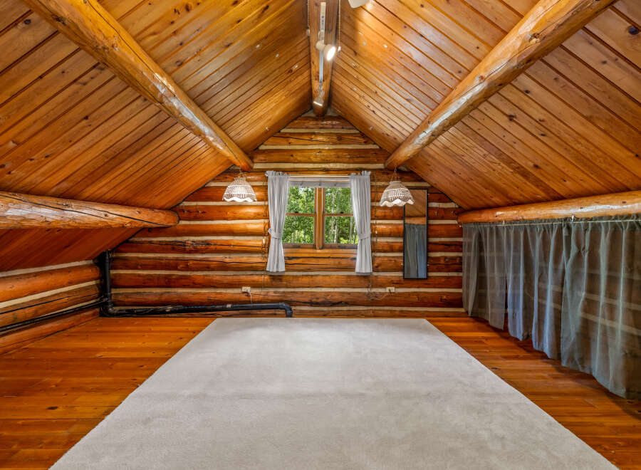 Experience rustic charm in this unique log cabin loft, featuring a vaulted wood-paneled ceiling and exposed beams.