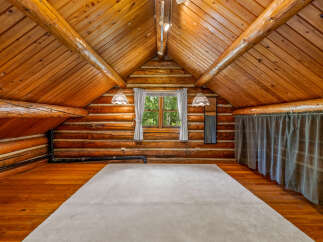 Experience rustic charm in this unique log cabin loft, featuring a vaulted wood-paneled ceiling and exposed beams.