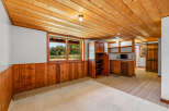 This charming basement living area features a cozy wood-paneled wainscoting and a warm, knotty pine ceiling.