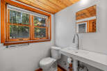 This charming bathroom features a rustic wooden ceiling and window frame, complemented by a modern white sink and toilet.