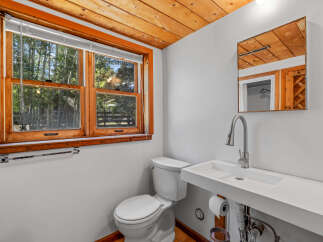 This charming bathroom features a rustic wooden ceiling and window frame, complemented by a modern white sink and toilet.