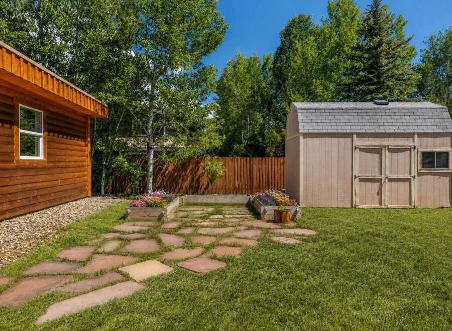 This charming backyard features a rustic wooden cabin and a practical storage shed, perfect for outdoor enthusiasts.