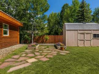 This charming backyard features a rustic wooden cabin and a practical storage shed, perfect for outdoor enthusiasts.