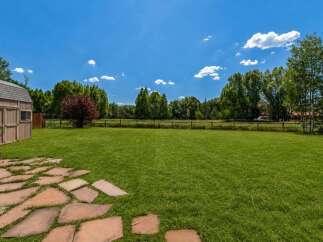 Enjoy the expansive green lawn perfect for outdoor activities and relaxation, bordered by a charming wooden fence and mature trees.