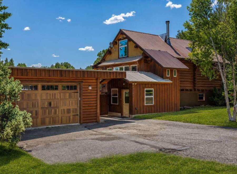 Experience rustic charm with this beautiful log home featuring a spacious wooden garage and a welcoming covered entryway.