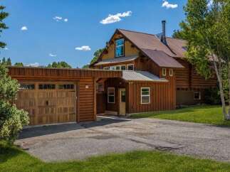 Experience rustic charm with this beautiful log home featuring a spacious wooden garage and a welcoming covered entryway.