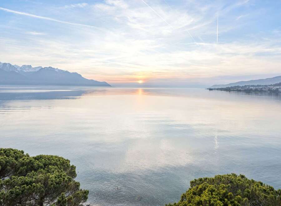 Experience breathtaking lakefront living with panoramic views of snow-capped mountains and a serene sunset.