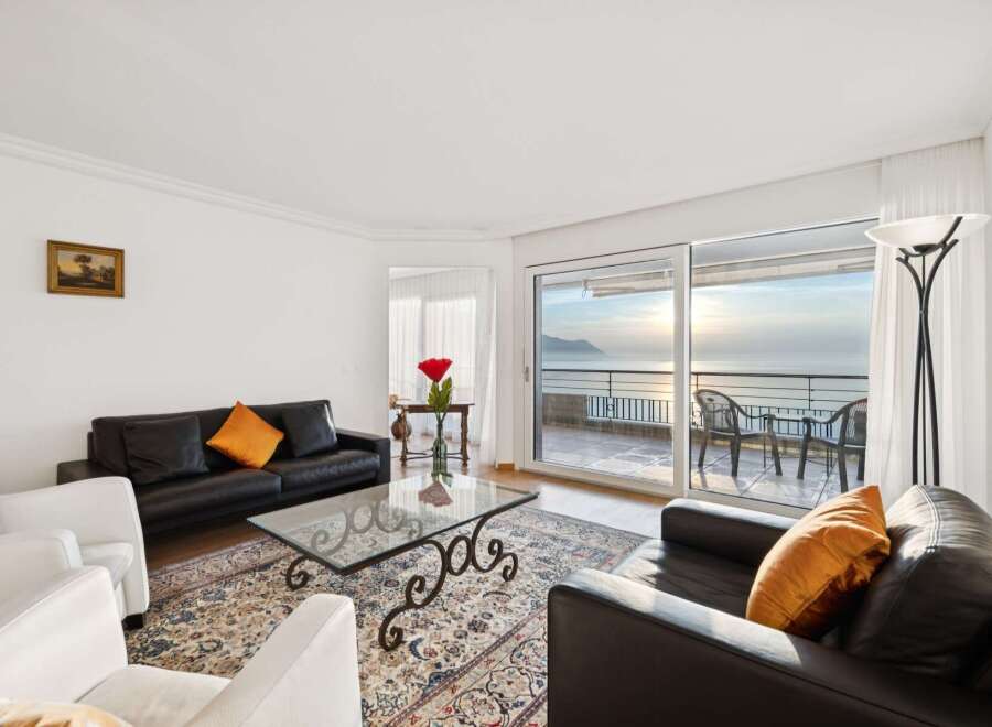 Experience breathtaking lake views from this elegant living room, featuring a sleek black leather sofa and a stylish glass coffee table.