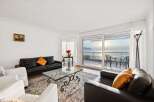 Experience breathtaking lake views from this elegant living room, featuring a sleek black leather sofa and a stylish glass coffee table.
