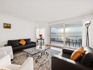 Experience breathtaking lake views from this elegant living room, featuring a sleek black leather sofa and a stylish glass coffee table.