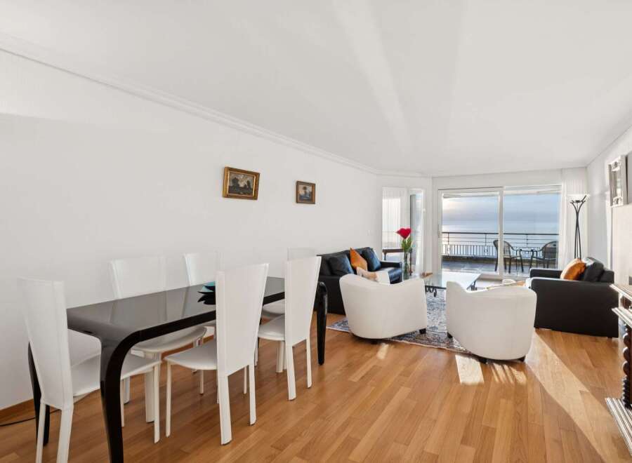 Experience breathtaking ocean views from this stunning living and dining area, featuring a sleek black dining table with white chairs and a comfortable seating arrangement.
