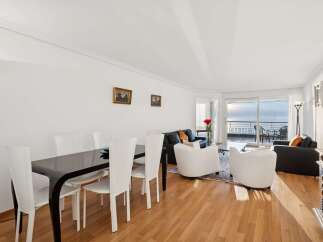 Experience breathtaking ocean views from this stunning living and dining area, featuring a sleek black dining table with white chairs and a comfortable seating arrangement.