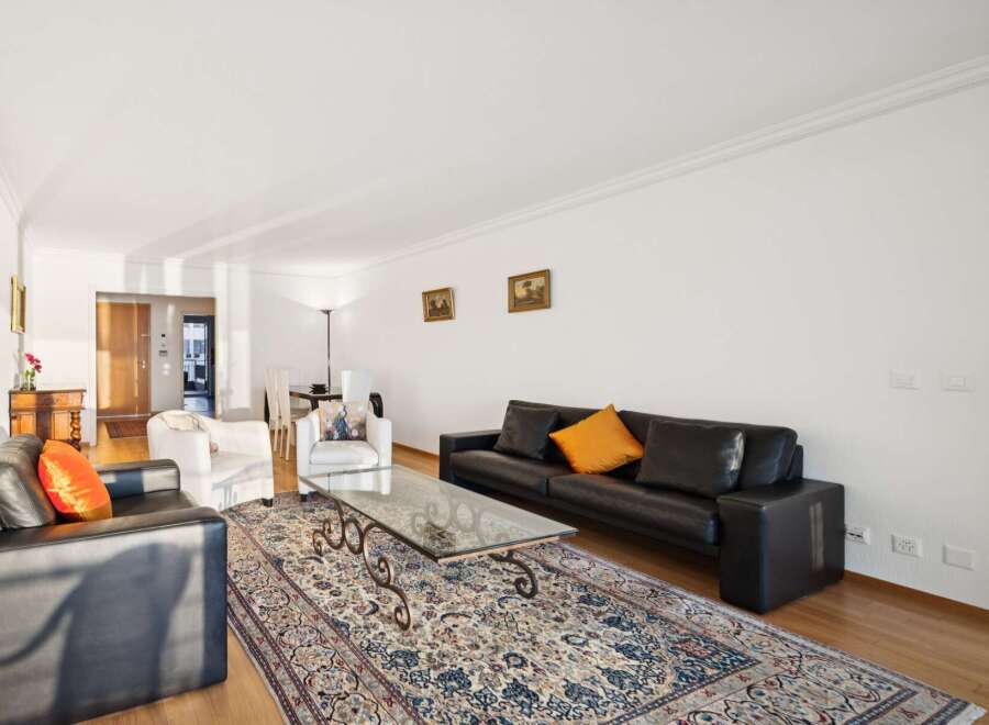 Experience elegant living in this spacious apartment, featuring a sophisticated black leather sofa and plush white armchairs perfect for relaxation.