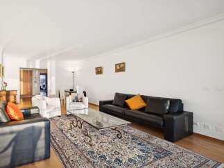 Experience elegant living in this spacious apartment, featuring a sophisticated black leather sofa and plush white armchairs perfect for relaxation.