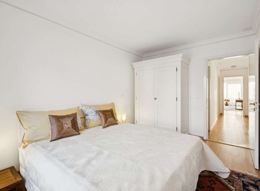 Experience comfort and style in this inviting bedroom, featuring a plush white bed adorned with decorative pillows and a large white wardrobe for ample storage.
