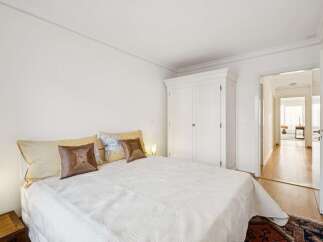 Experience comfort and style in this inviting bedroom, featuring a plush white bed adorned with decorative pillows and a large white wardrobe for ample storage.