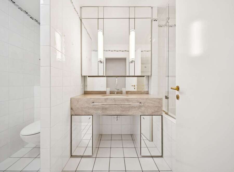This modern bathroom features a sleek marble vanity with a built-in sink and a large mirrored cabinet above.
