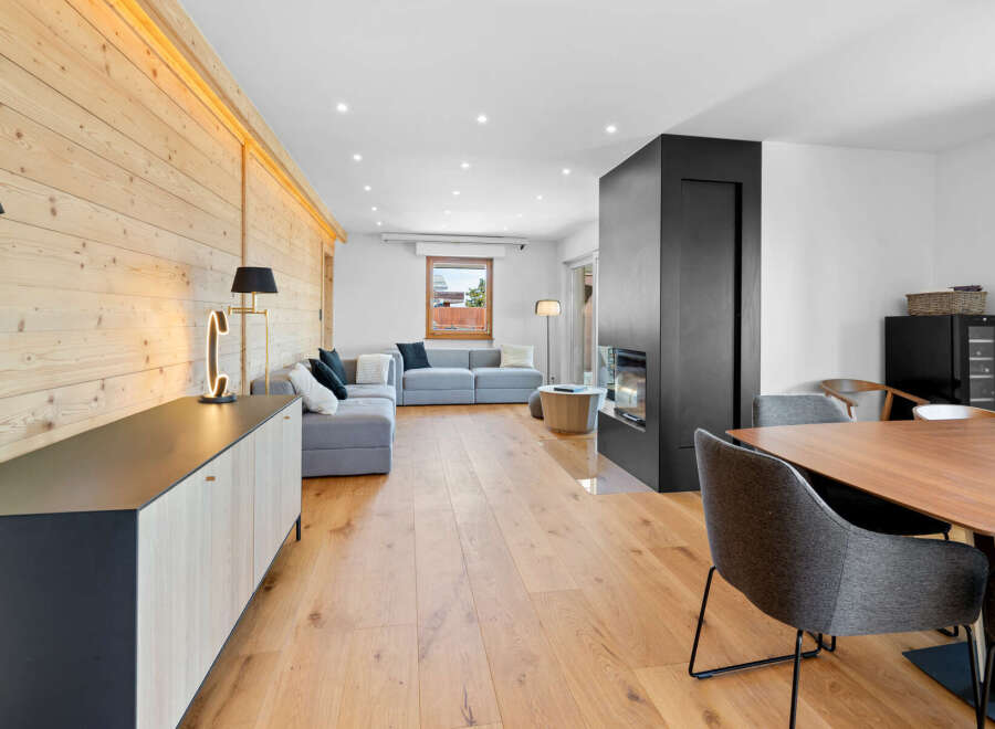 Experience modern living in this beautifully appointed living space, featuring a sleek grey sectional sofa complemented by a striking wood-paneled accent wall.