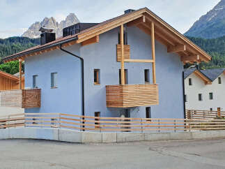 Experience modern alpine living in this stunning property featuring a light blue stucco exterior and a prominent wooden balcony.