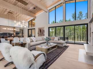 Experience luxury mountain living in this stunning home featuring a spacious open-concept living area with soaring ceilings and a wall of windows showcasing breathtaking forest views.