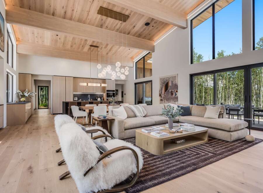 Experience modern luxury in this stunning open-concept living space, featuring a vaulted wood-beamed ceiling and expansive windows that flood the room with natural light.