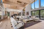 Experience modern luxury in this stunning open-concept living space, featuring a vaulted wood-beamed ceiling and expansive windows that flood the room with natural light.