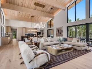 Experience modern luxury in this stunning open-concept living space, featuring a vaulted wood-beamed ceiling and expansive windows that flood the room with natural light.