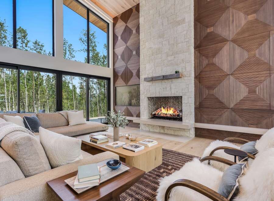 Experience luxury living in this stunning modern living room, featuring a grand stone fireplace and a dramatic floor-to-ceiling window wall overlooking a serene forest.