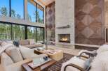 Experience luxury living in this stunning modern living room, featuring a grand stone fireplace and a dramatic floor-to-ceiling window wall overlooking a serene forest.