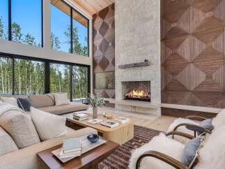 Experience luxury living in this stunning modern living room, featuring a grand stone fireplace and a dramatic floor-to-ceiling window wall overlooking a serene forest.