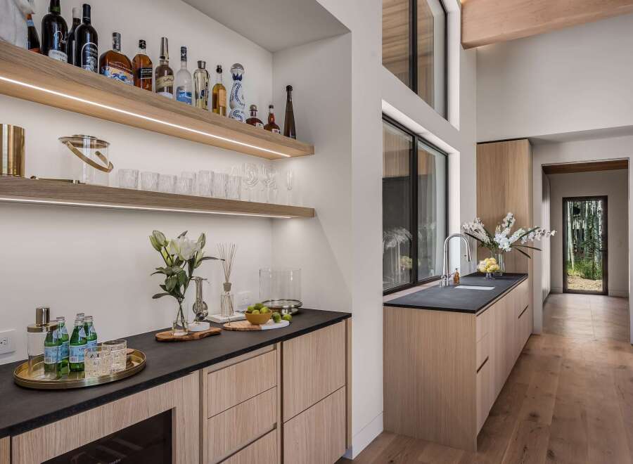 This modern home bar features sleek wooden cabinetry and floating shelves stocked with a variety of spirits and glassware.
