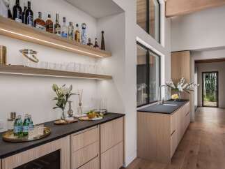 This modern home bar features sleek wooden cabinetry and floating shelves stocked with a variety of spirits and glassware.