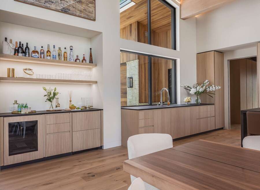 Experience sophisticated entertaining in this modern home featuring a sleek wet bar with a wine fridge and ample shelving for spirits.