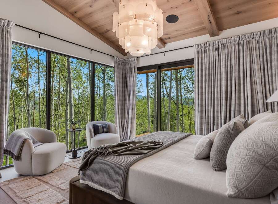 Experience luxury mountain living in this stunning bedroom, featuring floor-to-ceiling windows that offer breathtaking views of the surrounding aspen forest.