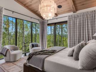 Experience luxury mountain living in this stunning bedroom, featuring floor-to-ceiling windows that offer breathtaking views of the surrounding aspen forest.